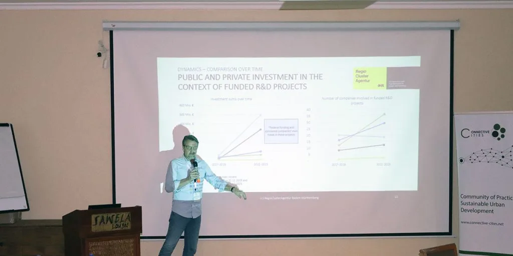 An expert stands next to a screen showing a PowerPoint presentation.